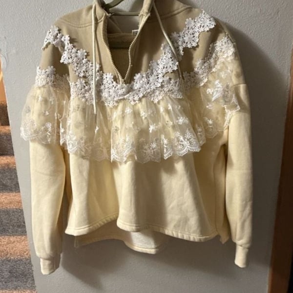 Beige or sand-colored zip-up sweatshirt white lace trim and a frilled lace hem.